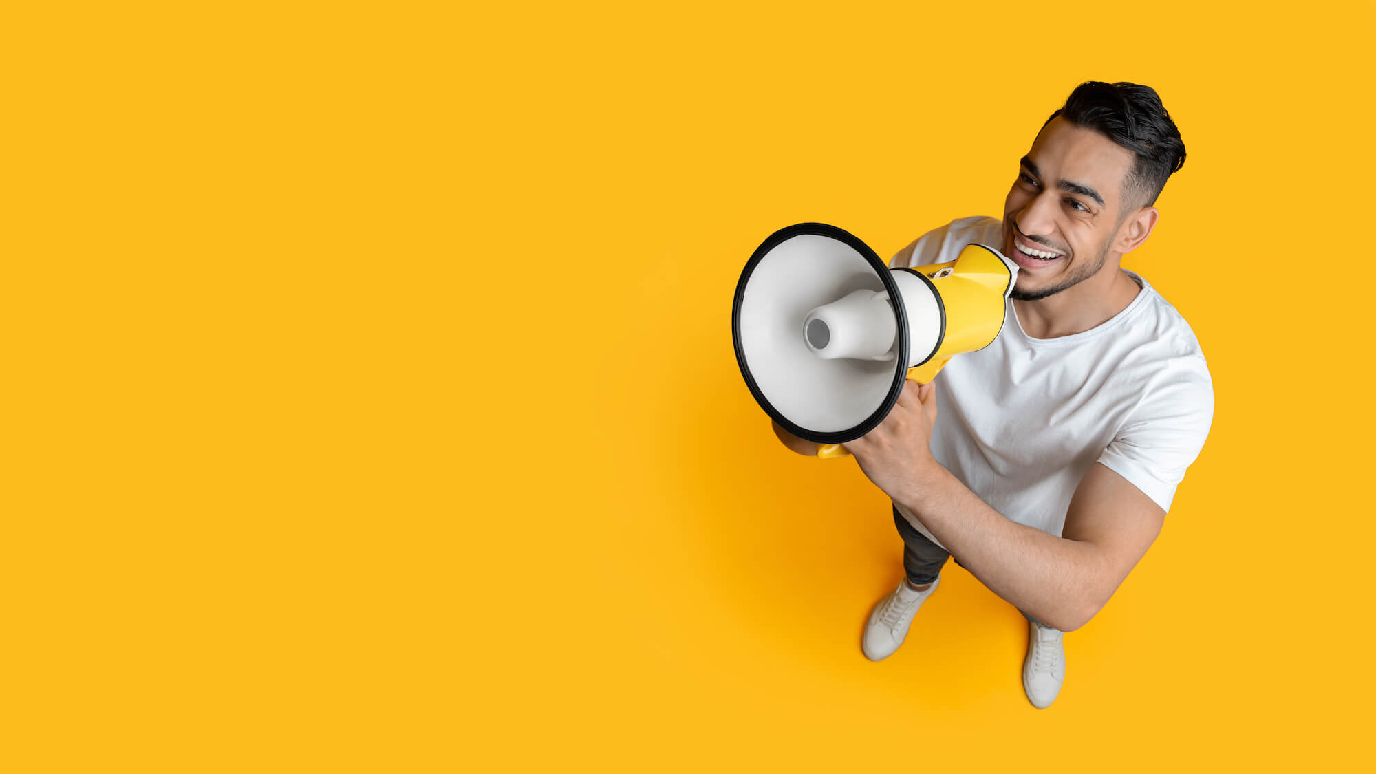 Smiling man holding a megaphone set against a yellow background