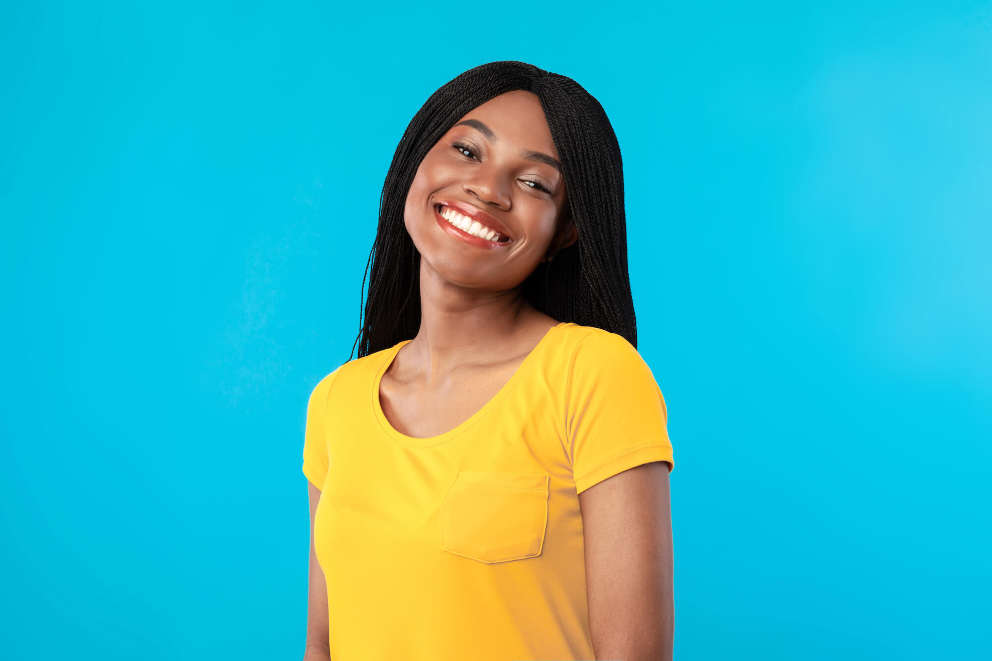 Woman in yellow shirt smiling at the camera in front of a blue background.