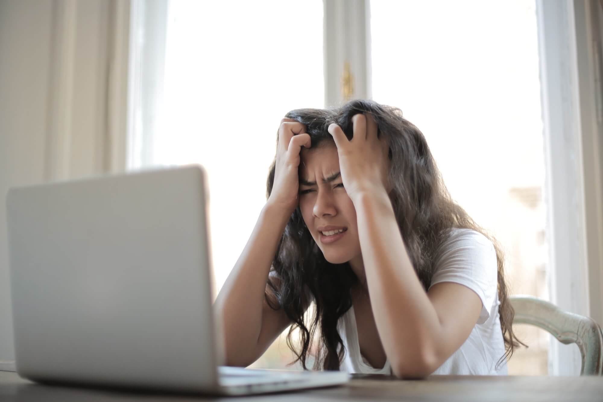 Frustrated woman at a desk clutching her head and leaning over a laptop.