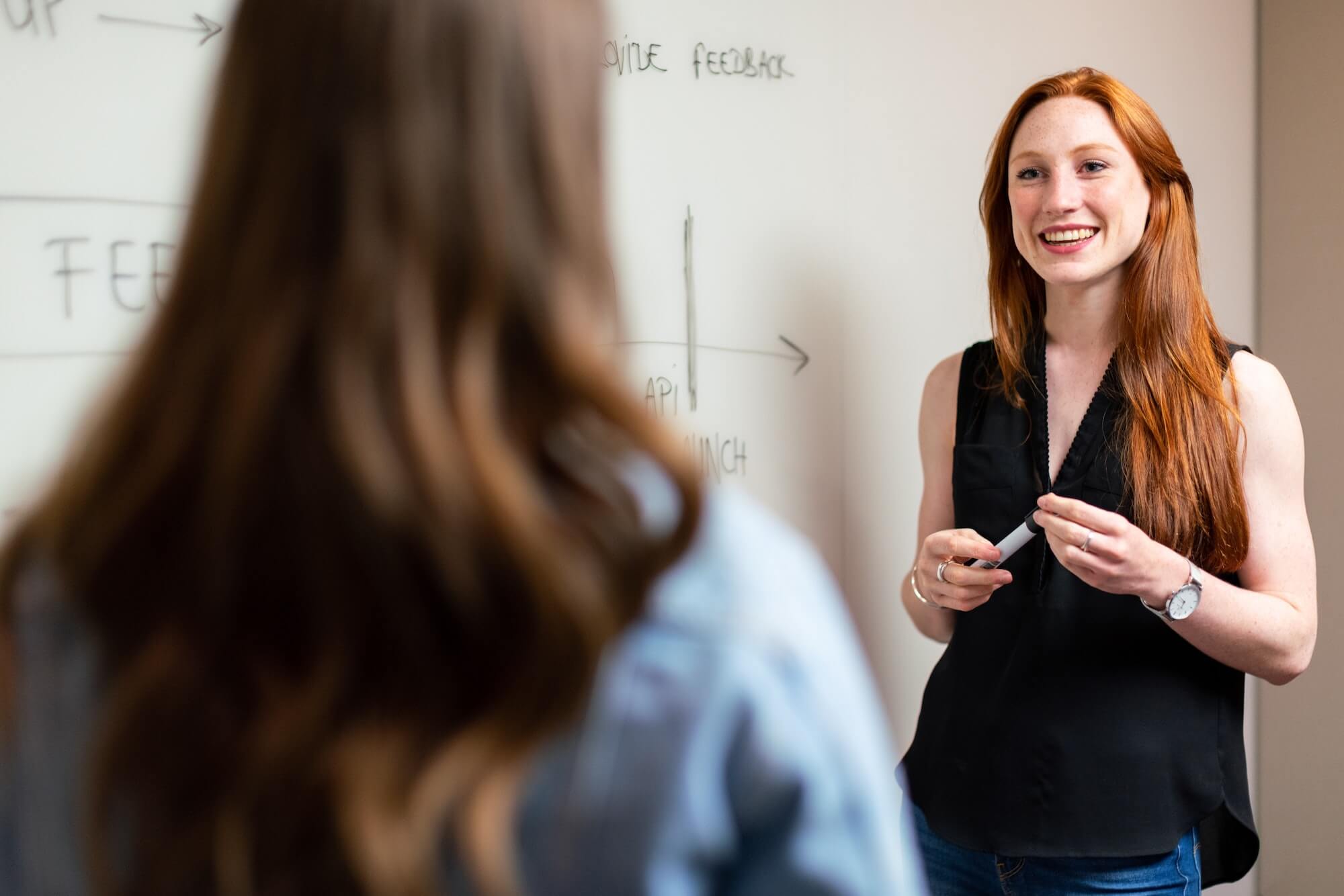 woman smiling in front of whiteboard talking to colleague