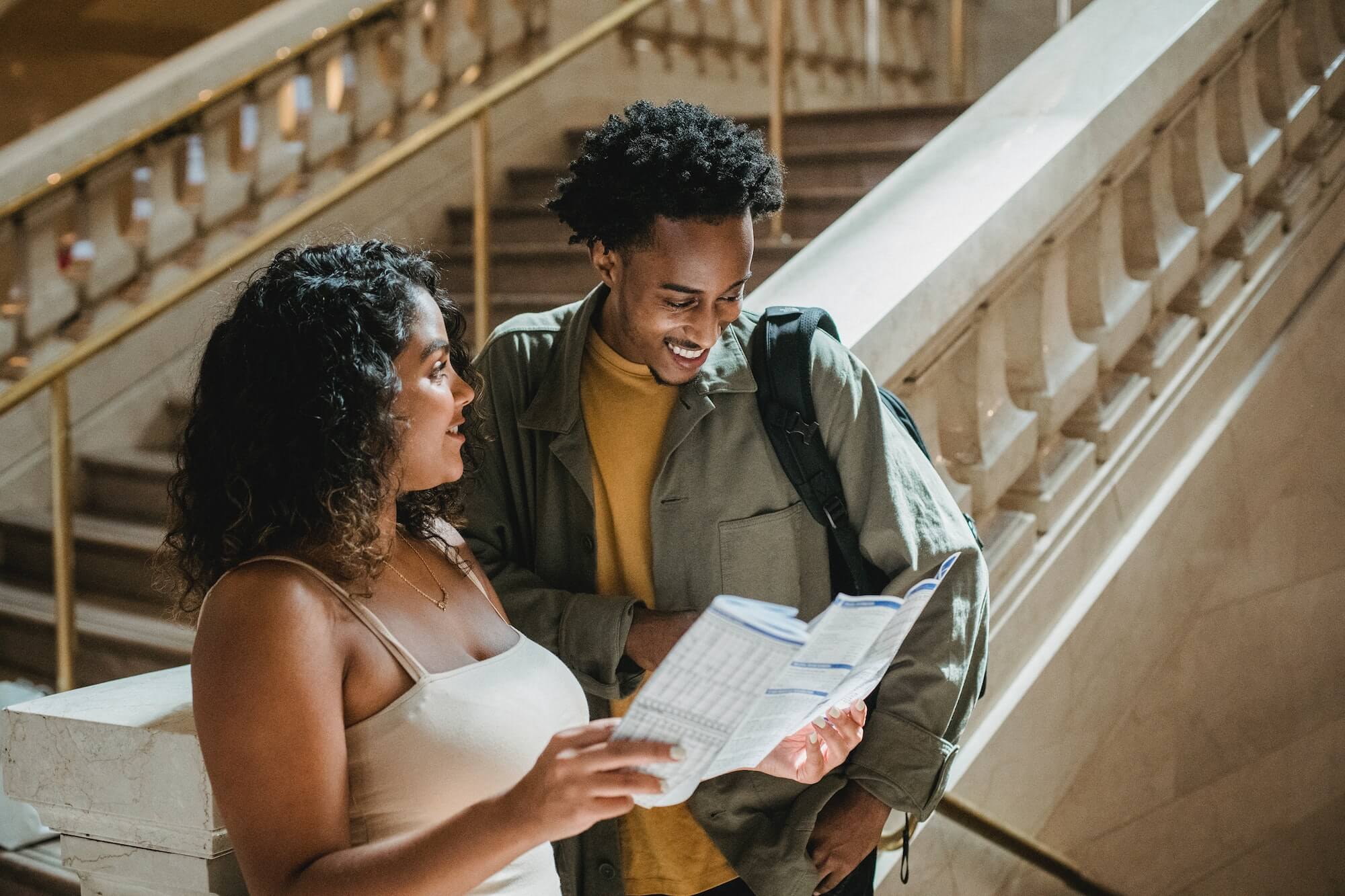 Woman standing by a staircase presenting a map to a man who is pointing at the map and talking to her.