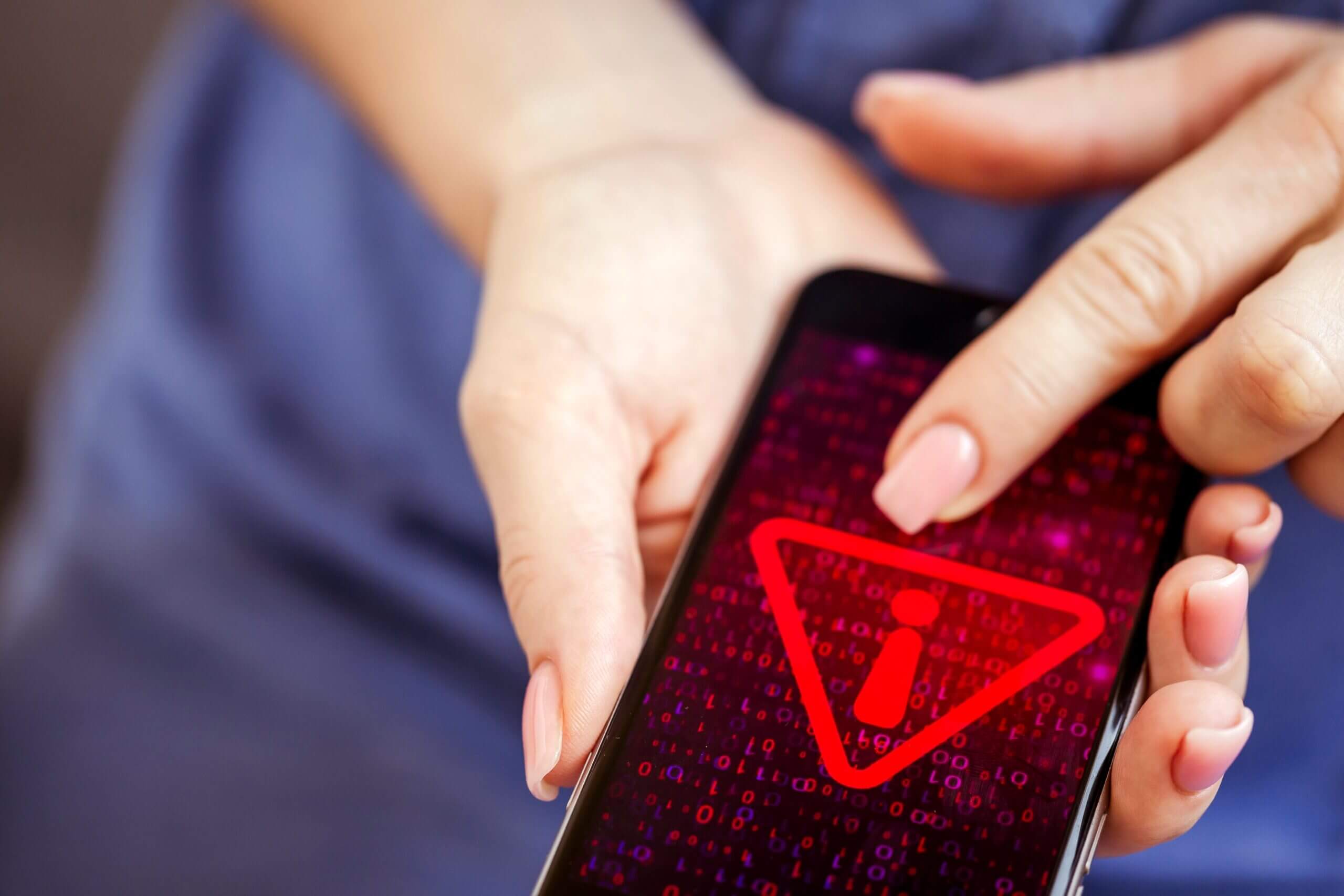 woman's hands holding a smartphone displaying a triangular red cybersecurity warning sign