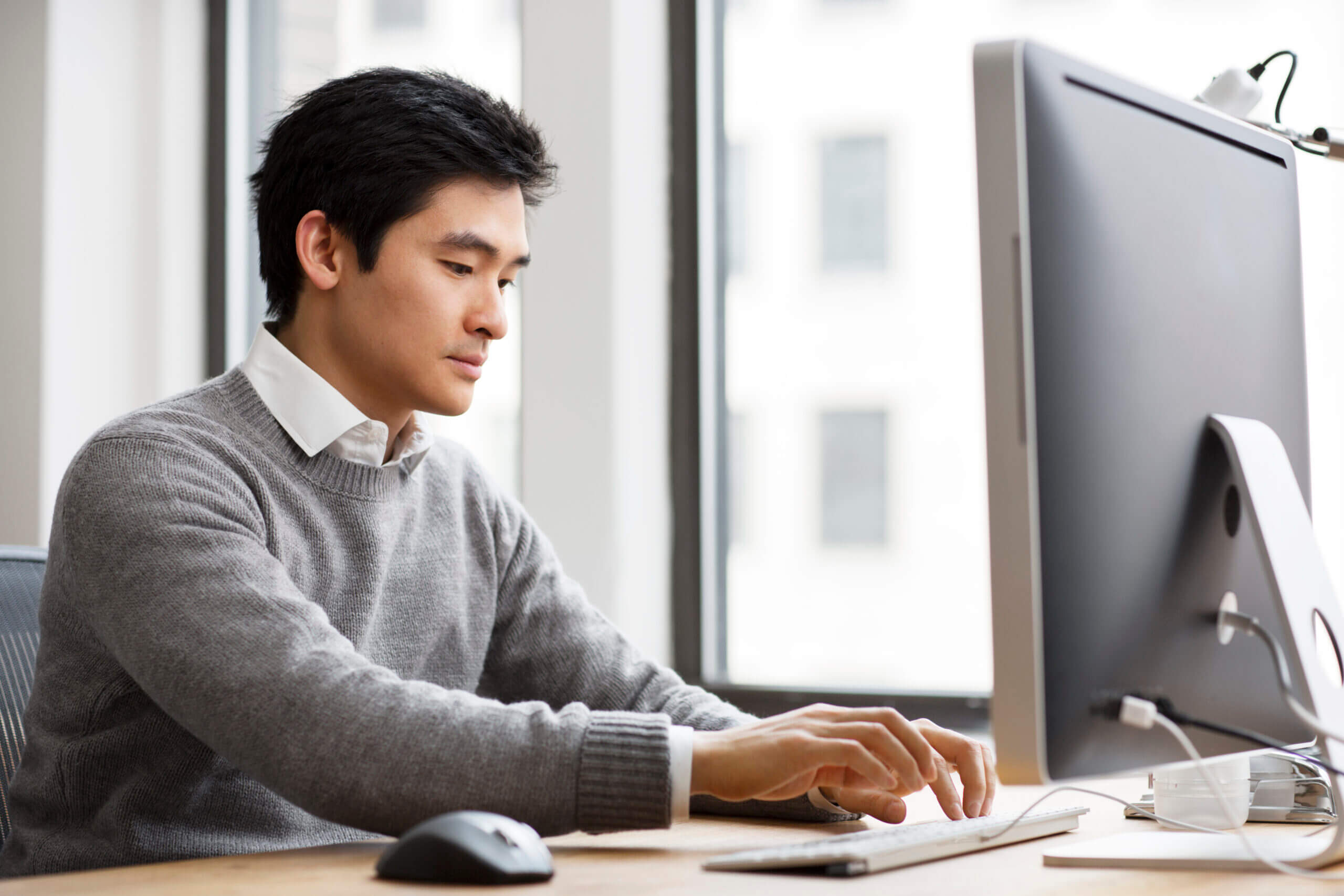 Man in sweater typing on desktop computer at work