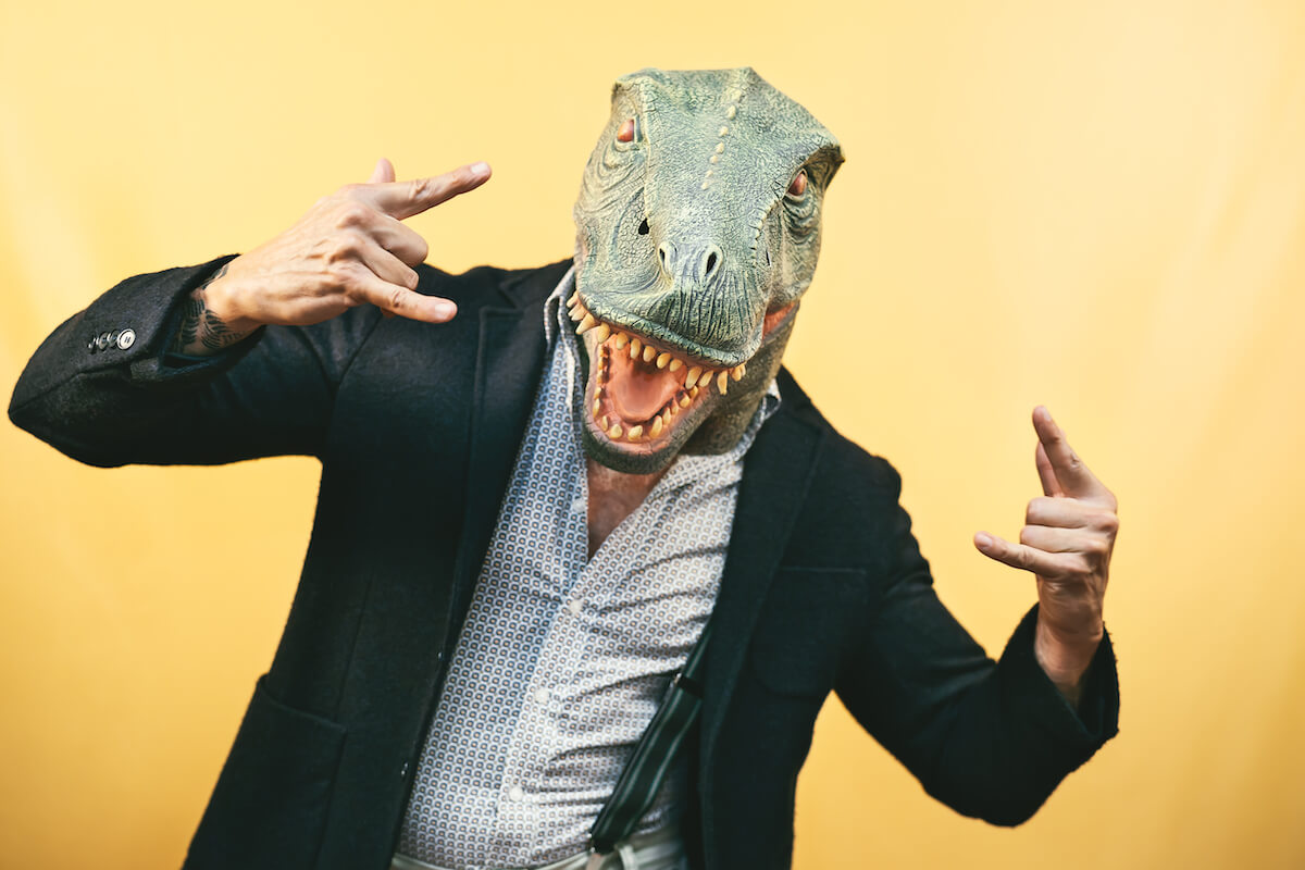 A man wearing a reptile mask over his head with this hands up. 