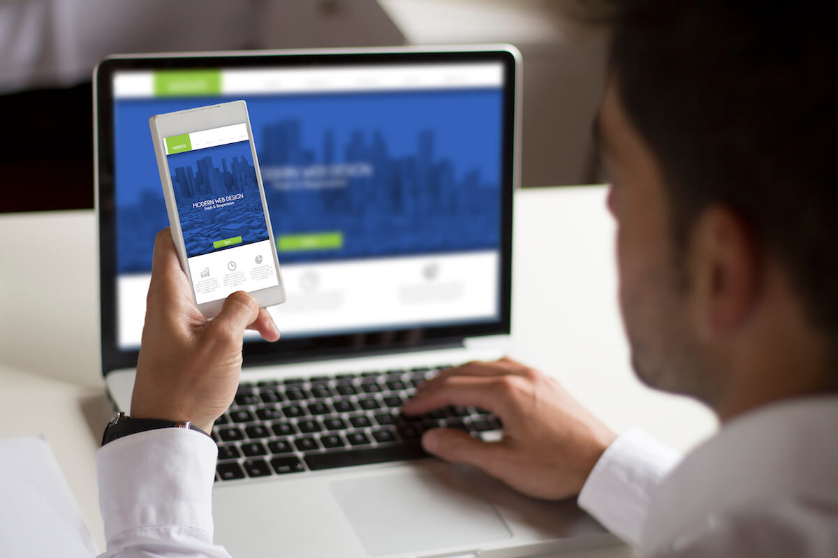 A man testing a website on his laptop and phone at the same time. 