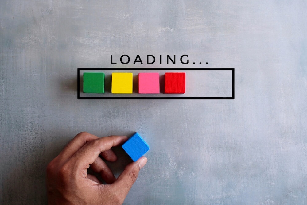 The word "loading" with four colorful blocks in a loading bar and a person holding one of the blocks.