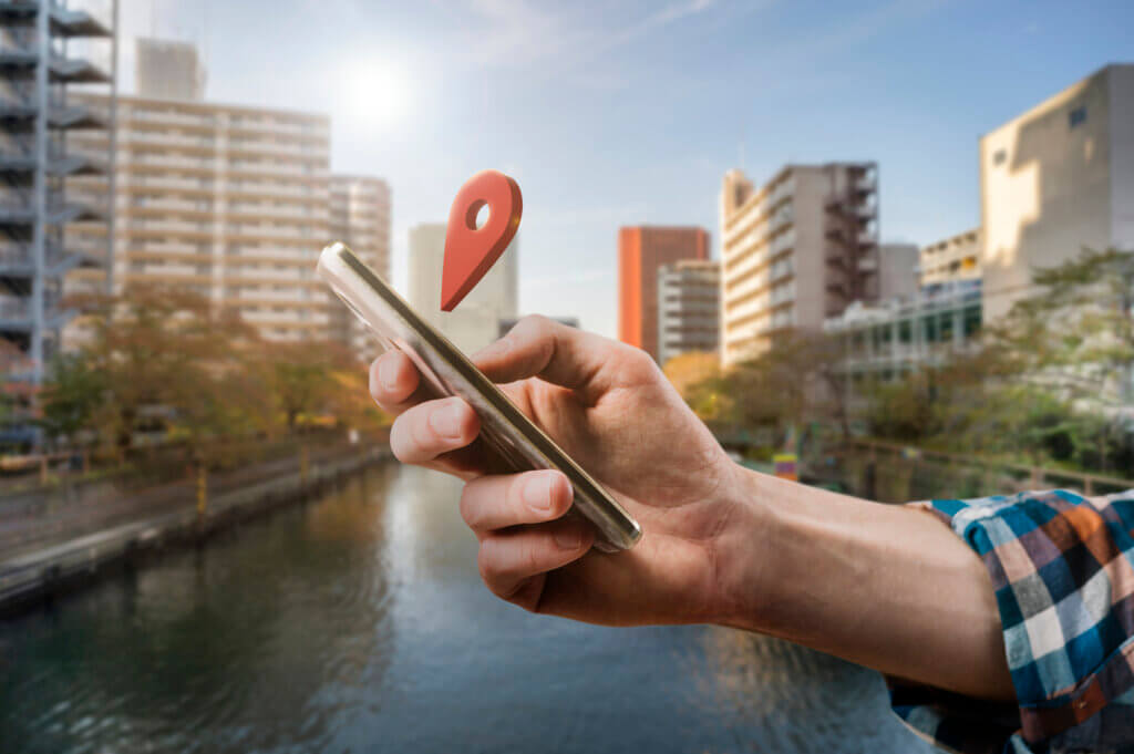 Man holding a smartphone with a geo pin hovering over it.